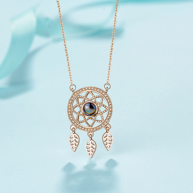Real rose-gold dreamcatcher projection necklace on a pale blue background